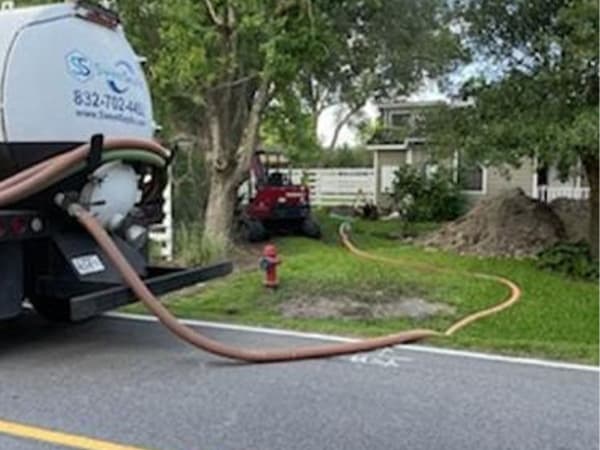 On-site septic pumping and maintenance services across the Houston area Septic service truck performing tank pumping with extended hose at a Houston property